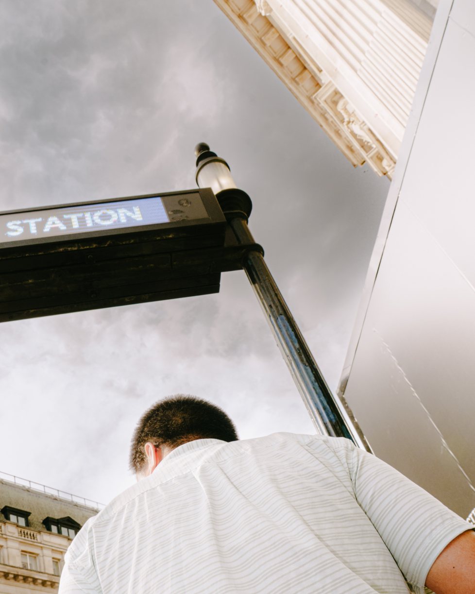 Print: a man in a striped shirt climbing out beneath a Station sign