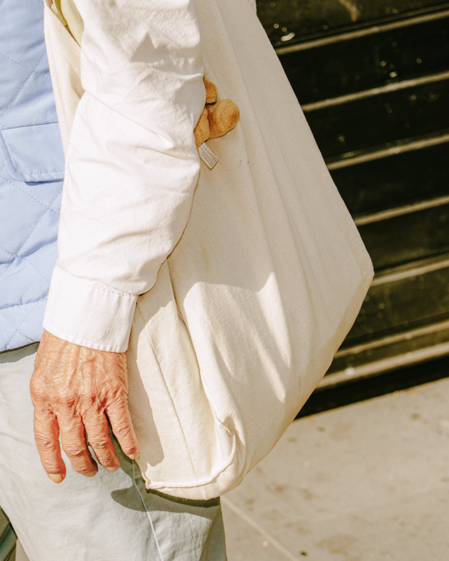 An older hand at the cuff of a white shirt, a canvas tote over the shoulder